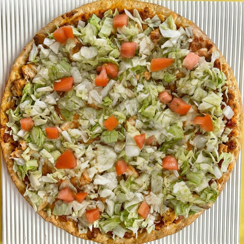 A whole taco pizza, topped with shredded lettuce, diced tomatoes, and chicken.