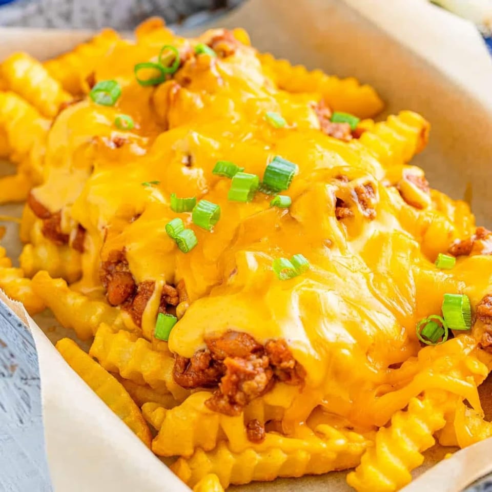Close-up of golden crinkle-cut fries generously topped with melted cheese, chili, and chopped green onions.