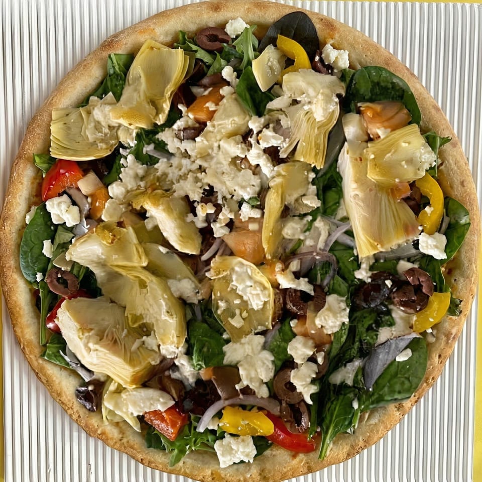 A vibrant Greek pizza with artichokes, olives, feta, spinach, and bell peppers on a crispy crust.