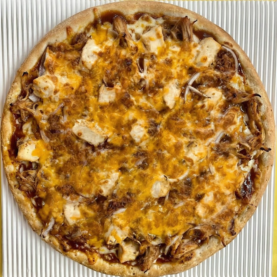 A whole BBQ chicken pizza with melted cheddar cheese, chicken pieces, and onions on a white ribbed surface.